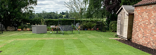 Large lawn garden. With a hedge, tress and seating in the background.