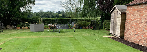 Large lawn garden. With a hedge, tress and seating in the background.